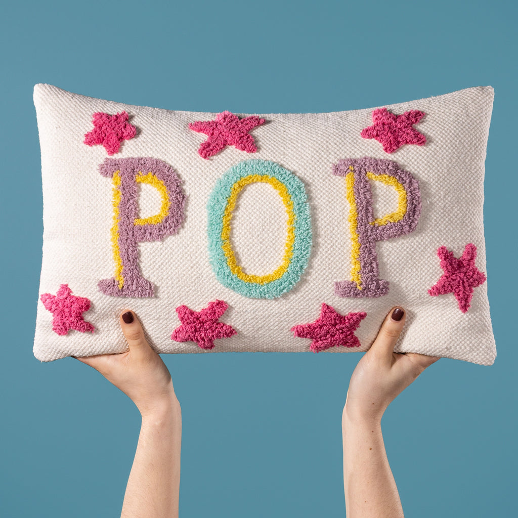 Cream rectangular cushion featuring colourful textured POP lettering and bright pink star details.