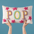 Cream rectangular cushion featuring colourful textured POP lettering and bright pink star details.