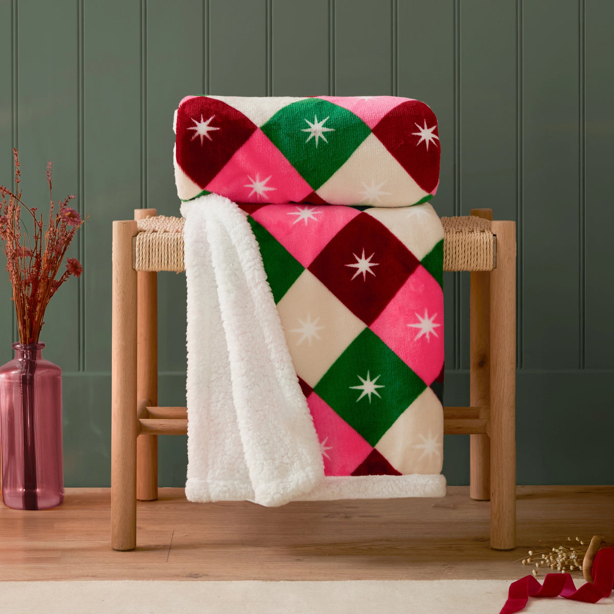 Colourful pink, red, green and cream checked throw with white stars and fluffy sherpa backing styled over a wooden chair.