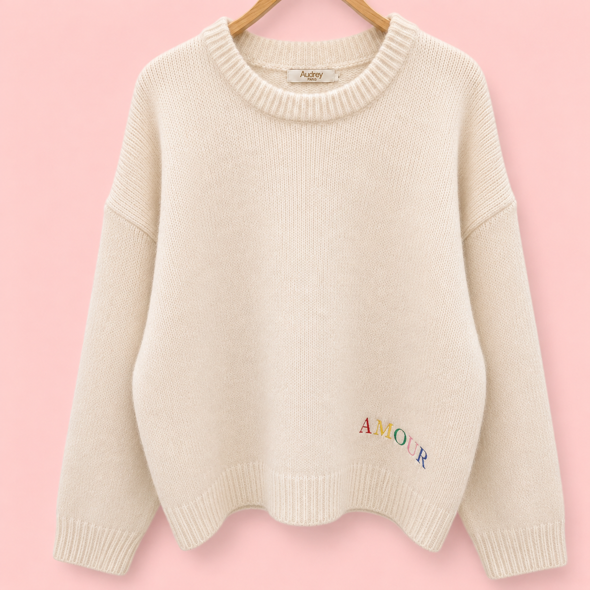 Front of cream knitted jumper with small multicoloured AMOUR embroidery near the hem.