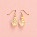 One of a kind gold plated drop earrings with translucent lemon glass heart beads, soft yellow beads and small gold star details on a peachy pink background.