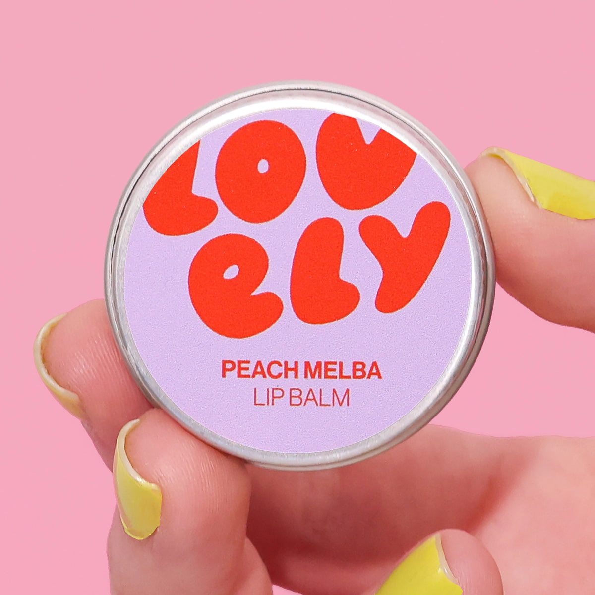 Peach Melba Lip Balm tin held in a hand against a pink background.