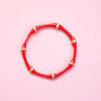 Red enamel bamboo style bangle with gold tone detailing on a pink background.