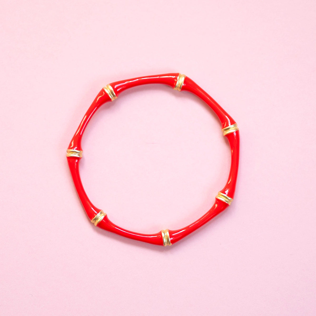 Red enamel bamboo style bangle with gold tone detailing on a pink background.