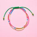 Adjustable three strand beaded bracelet with pink, turquoise, white and gold beads and a green cord fastening.
