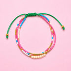 Adjustable three strand beaded bracelet with pink, turquoise, white and gold beads and a green cord fastening.