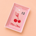 Pink rectangular trinket dish with vintage postage stamp design, red cherries and Mon Chéri lettering on a peach background.