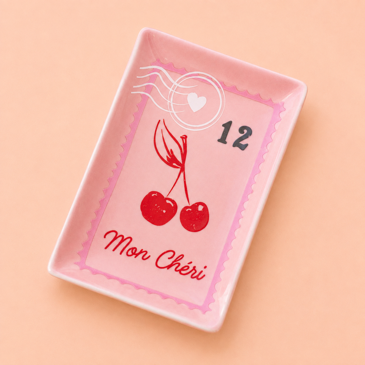 Pink rectangular trinket dish with vintage postage stamp design, red cherries and Mon Chéri lettering on a peach background.
