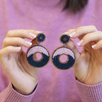 Pair of pink and navy circular beaded statement earrings held up to show their size and detailing.