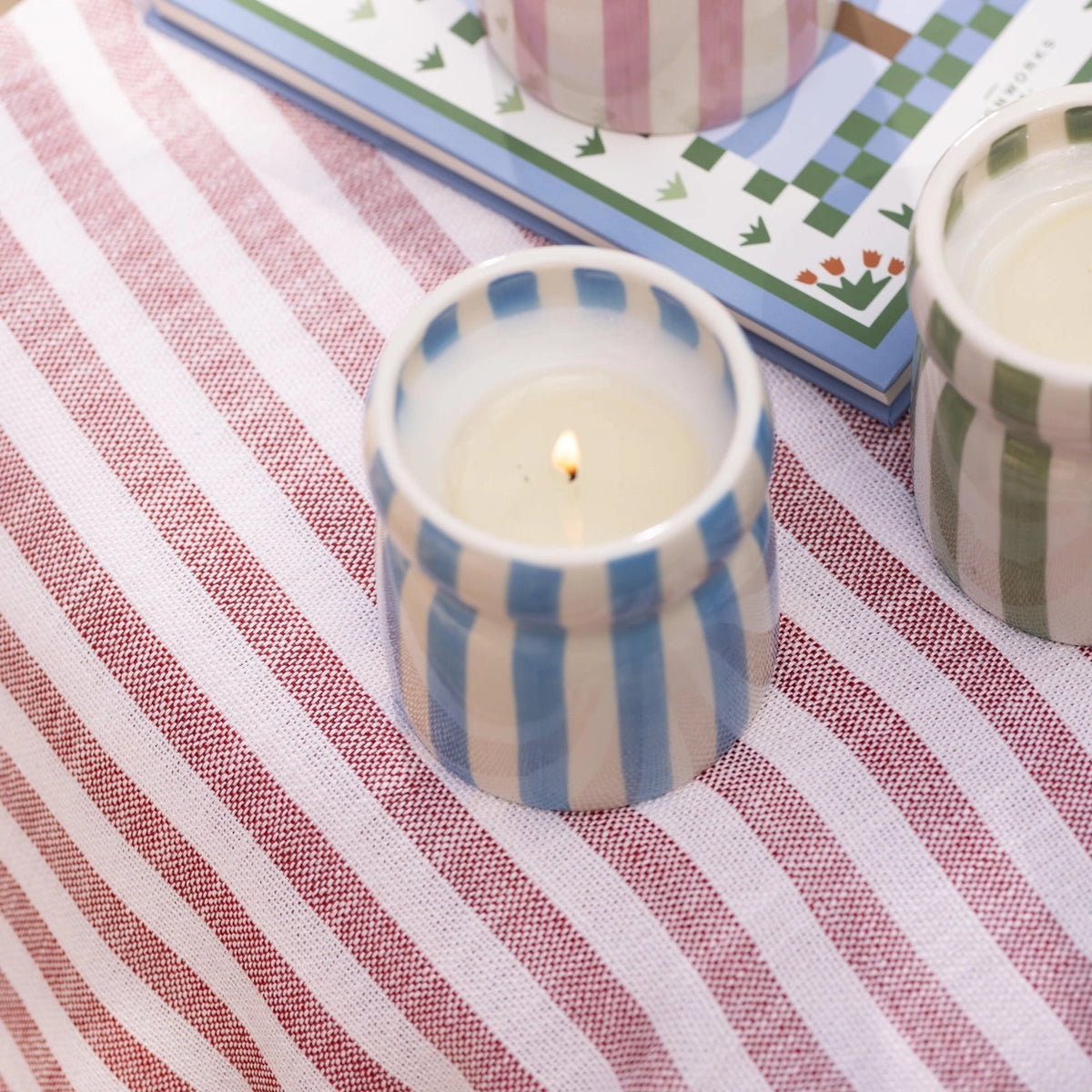 Blue striped Lost at Sea candle styled with pink and green striped ceramic candles on a colourful table.