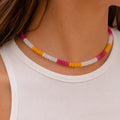 Woman wearing a colourful natural stone bead necklace with mango yellow, raspberry pink and white beads.