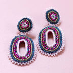 Pink and blue beaded oval statement earrings with layered seed bead detailing on a pale pink background.