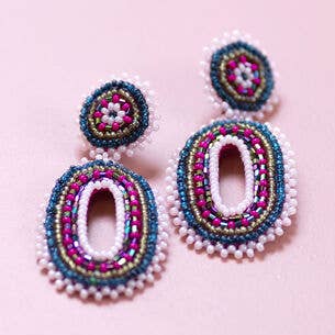 Pink and blue beaded oval statement earrings with layered seed bead detailing on a pale pink background.