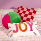 Colourful JOY tufted cushion styled on a patterned sofa with bright pink, green and checkerboard cushions.