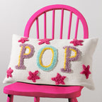 Cream rectangular POP cushion with colourful raised lettering and pink stars styled on a bright pink chair.