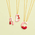 Pink and red enamel A, B and C initial necklaces with delicate gold-tone chains on a pale green background.