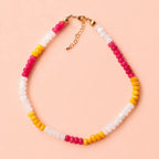 Colourful natural stone bead necklace with mango yellow, raspberry pink and white beads on a peach background.
