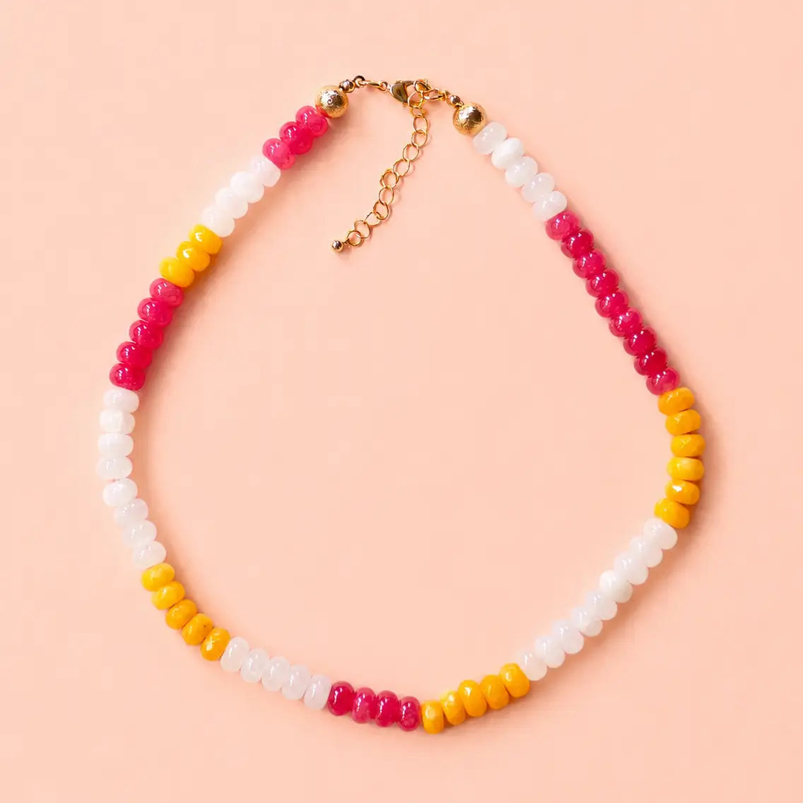 Colourful natural stone bead necklace with mango yellow, raspberry pink and white beads on a peach background.
