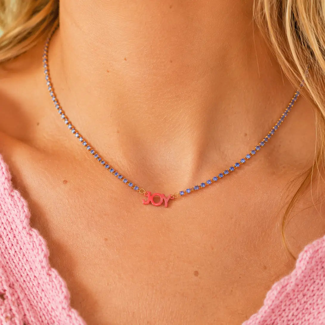 Woman wearing the Pocketful of Joy signature necklace with a blue crystal tennis chain and coral JOY charm.