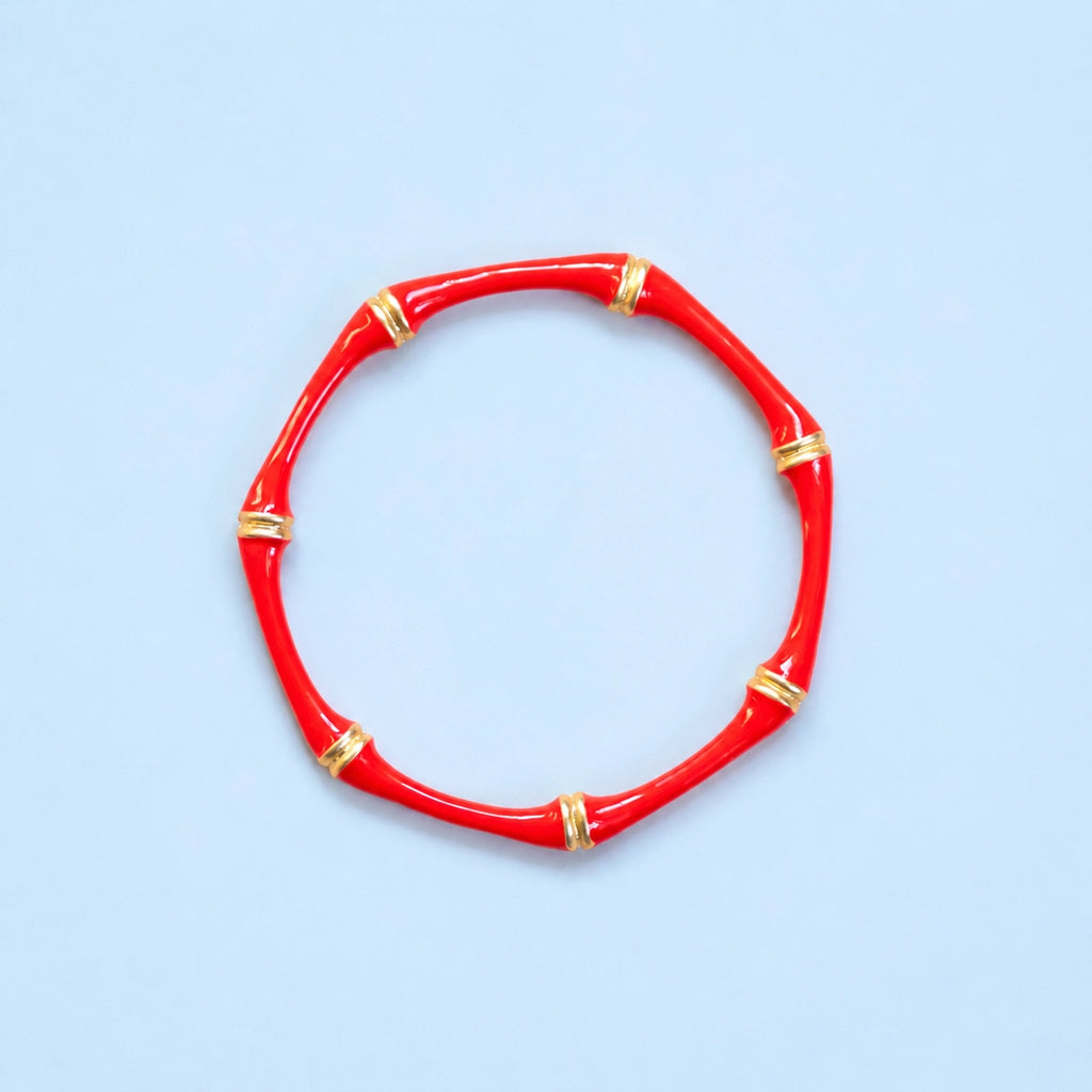 Glossy red enamel bamboo style bangle with gold tone accents on a blue background.