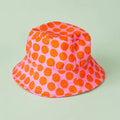 Pink bucket hat with bold orange polka dots against a pale green background.