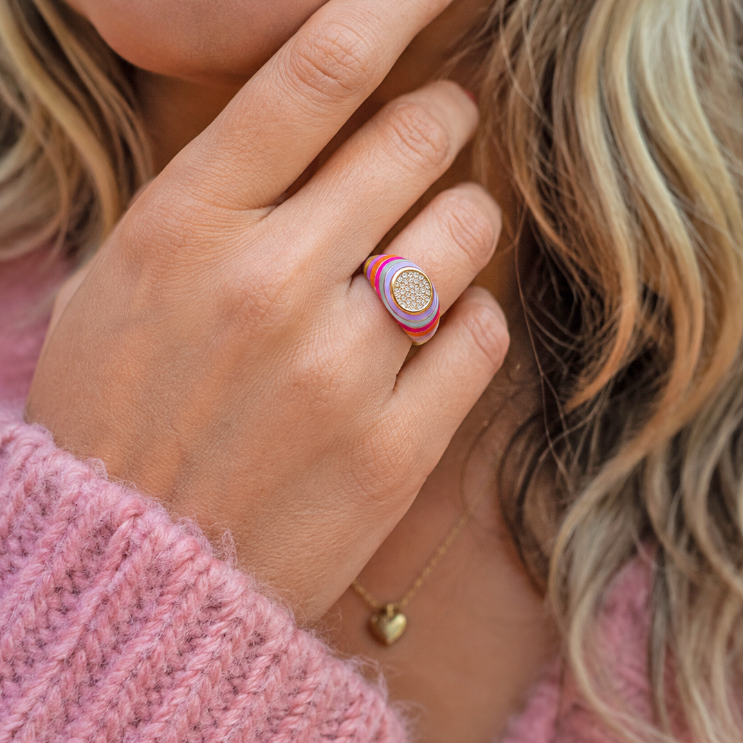 Close up of colourful striped enamel signet ring with round crystal set centre worn on a finger.