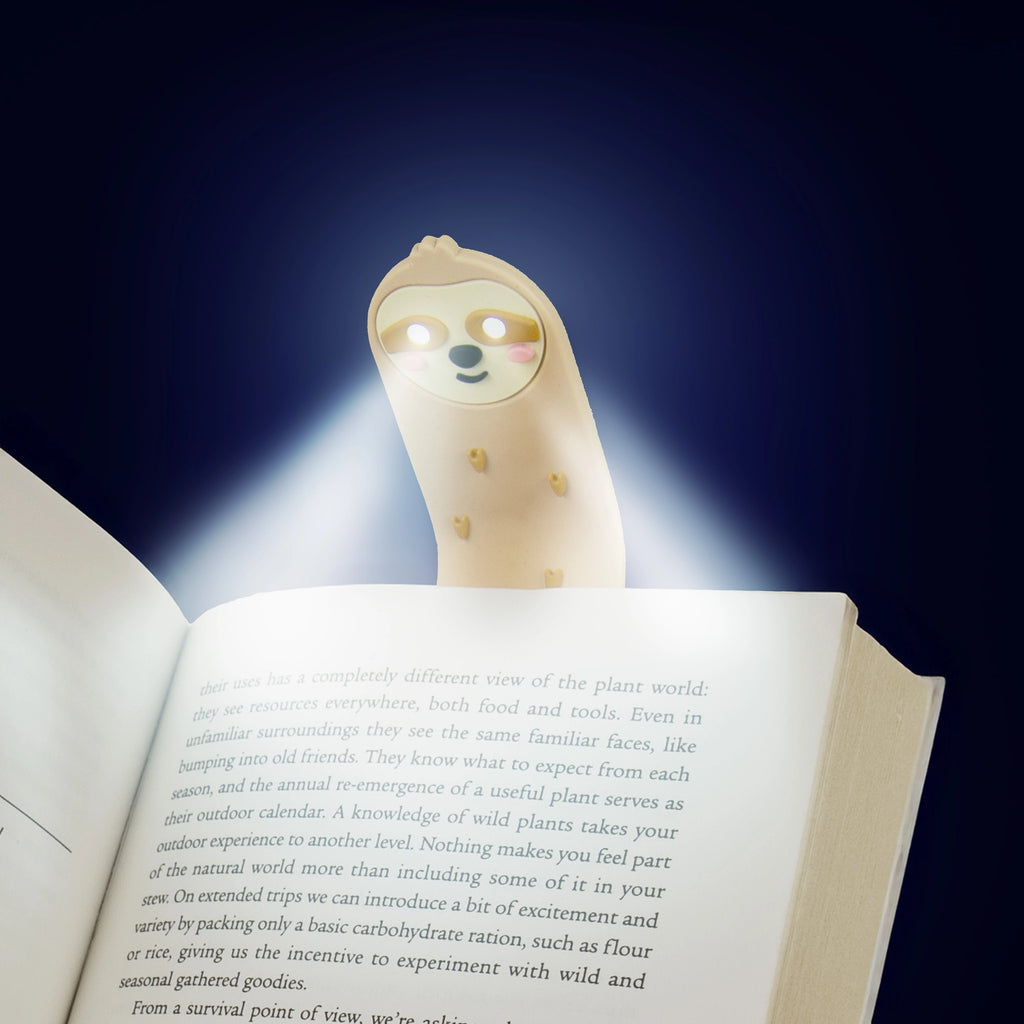 Sloth reading light glowing over the pages of an open book in the dark.
