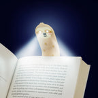 Sloth reading light glowing over the pages of an open book in the dark.
