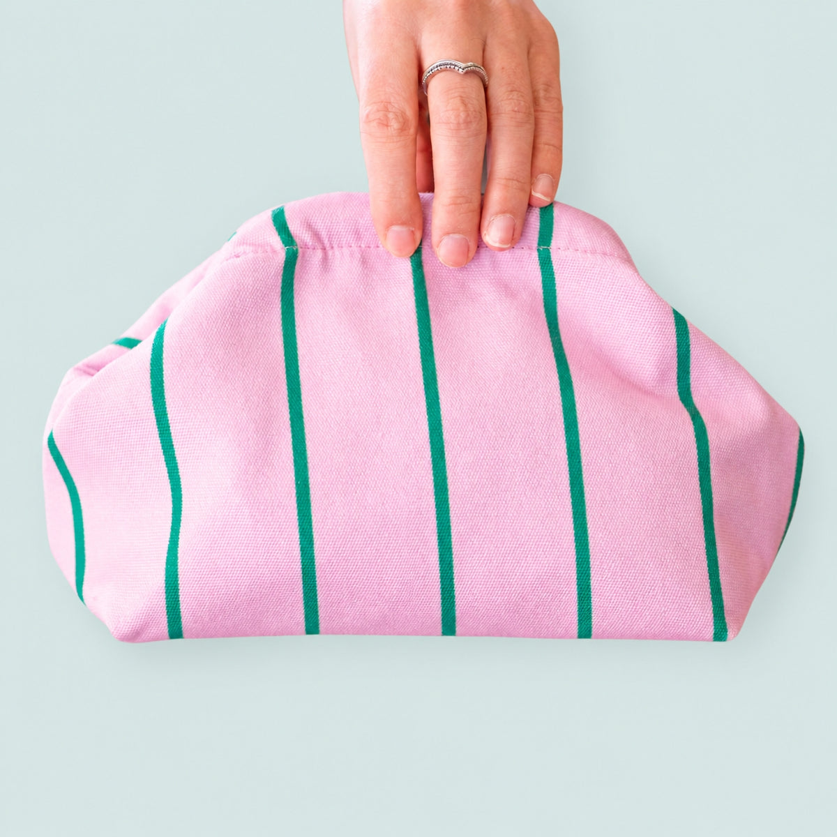 Cheerful pink and green striped multi use clutch bag shown close up against a fresh pale blue background.