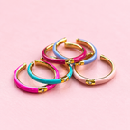 Pink, turquoise, lilac and pale pink enamel CZ rings showing their open band design on a soft pink background.