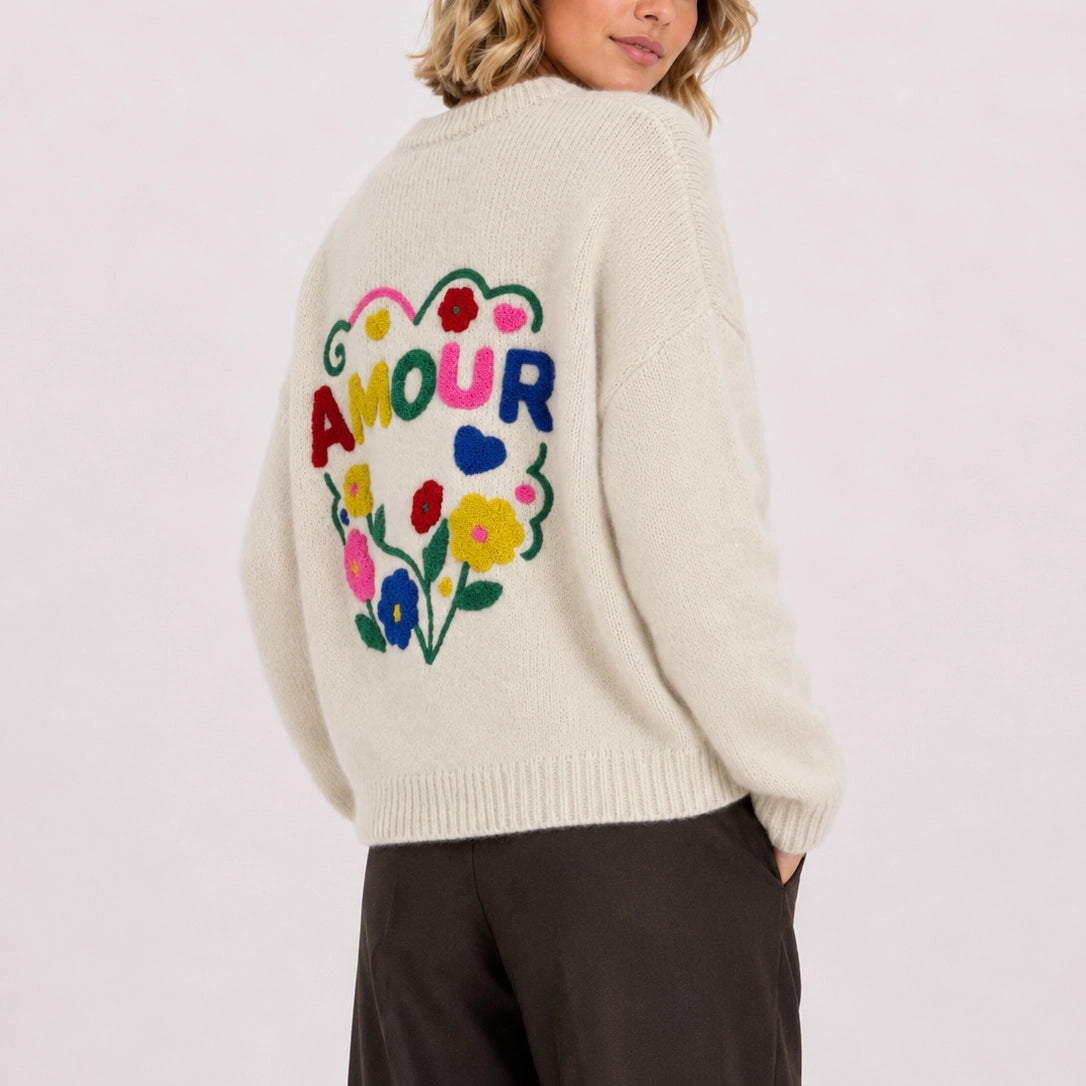 Woman wearing cream relaxed fit jumper showing the large colourful floral AMOUR embroidery on the back.