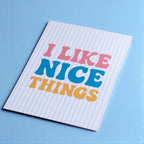 Cheerful I Like Nice Things A5 print with colourful retro lettering and pale pink stripes on a bright blue background.