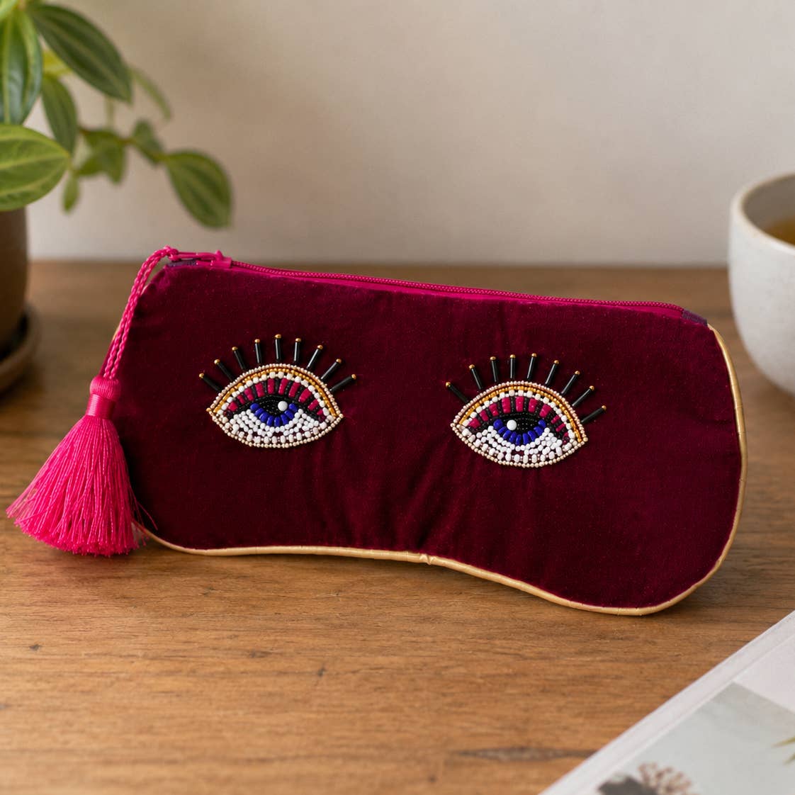 Burgundy velvet beaded eye glasses pouch with pink tassel displayed on a wooden table.