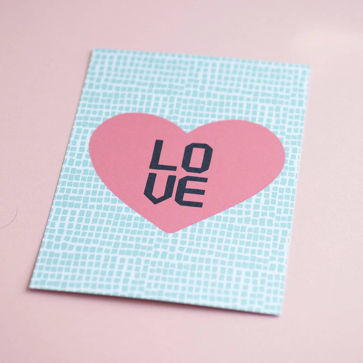 LOVE A5 art print featuring a bold pink heart and navy typography on a mint patterned background, photographed on soft pink.