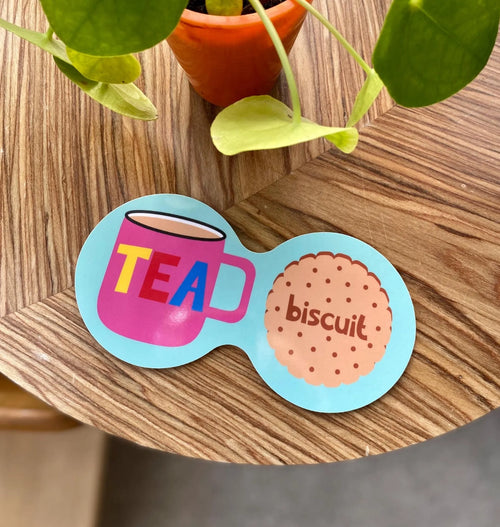 Aqua blue double coaster with bright pink tea mug, colourful TEA lettering and illustrated biscuit on a wooden table.