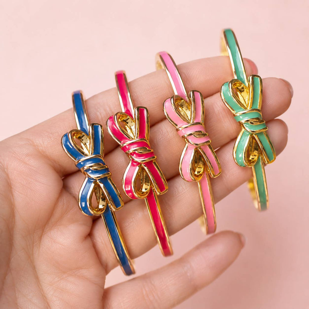 Blue, bright pink, pale pink and mint green enamel bow bangles held together against a soft pink background.