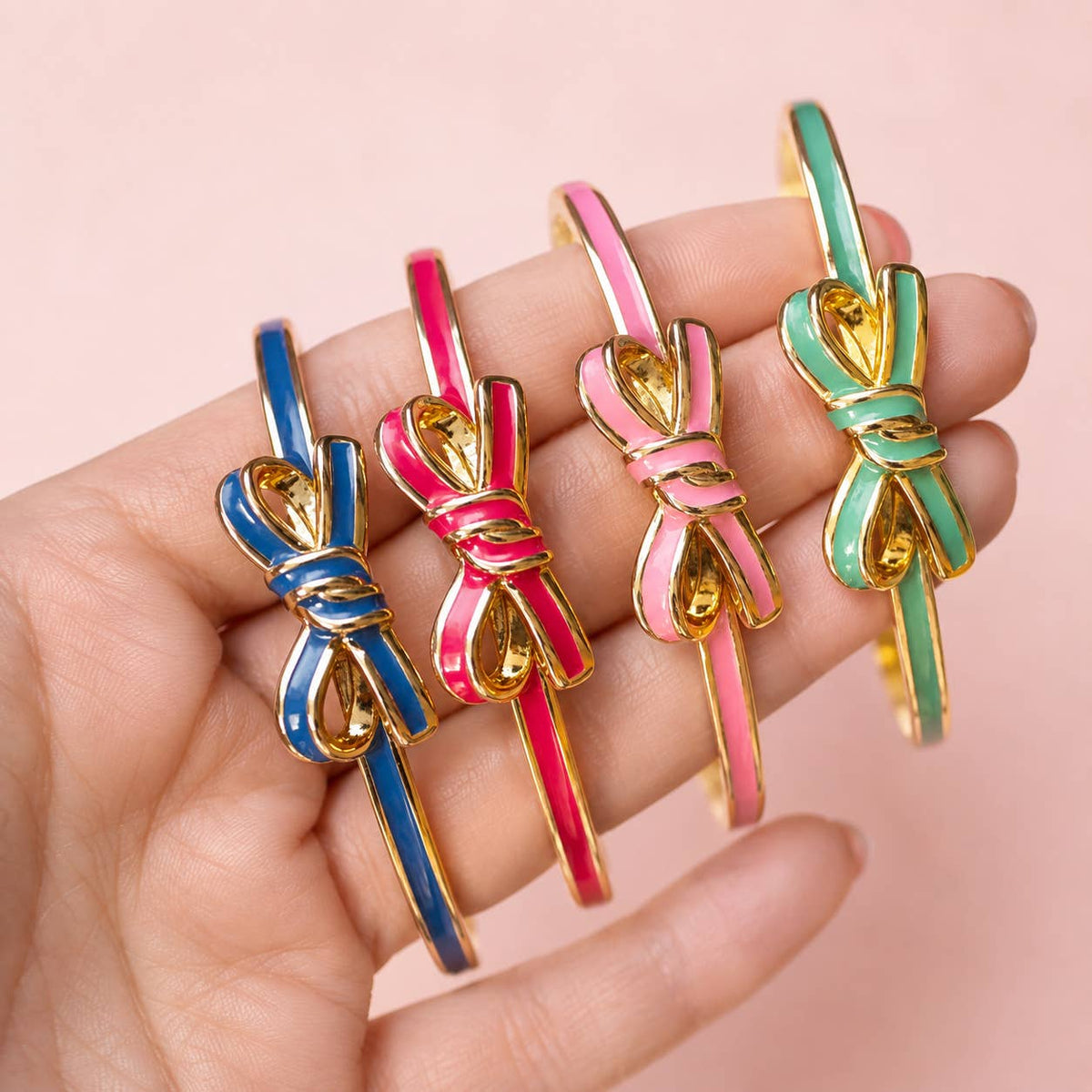 Blue, bright pink, pale pink and mint green enamel bow bangles held together against a soft pink background.