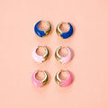 Three pairs of colourful enamel huggie hoop earrings in cobalt blue, pale pink and bright pink with gold-tone detailing.