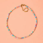 Colourful pastel natural stone bead necklace with genuine multicolour beads and a gold plated extension chain on a peach background.
