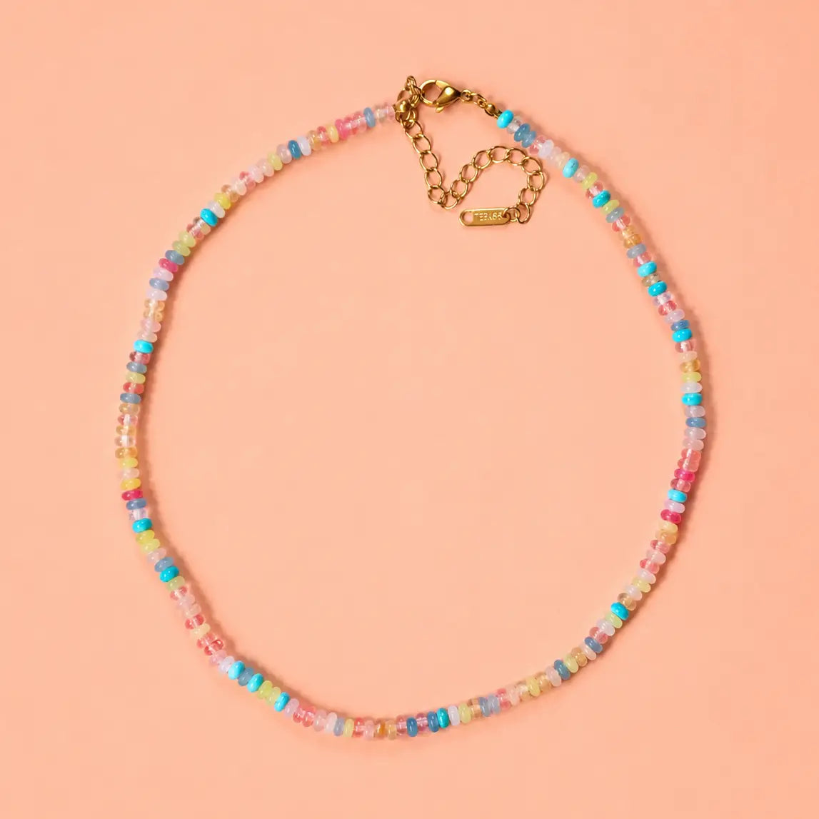 Colourful pastel natural stone bead necklace with genuine multicolour beads and a gold plated extension chain on a peach background.
