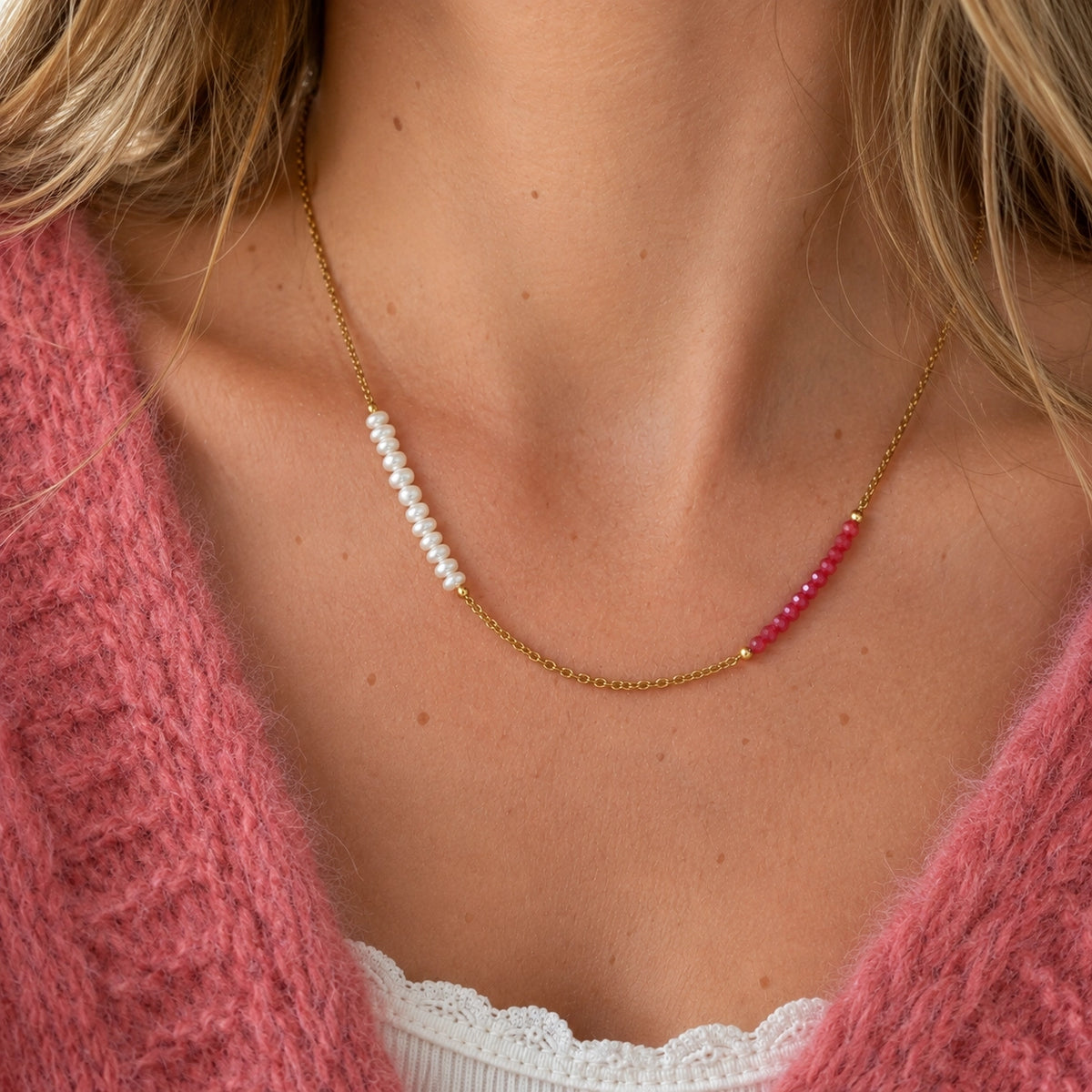 Strawberries and cream necklace worn with a pink knit, featuring a gold tone chain, white pearls and raspberry pink beads.