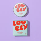 Vanilla Mint Lip Balm tin and colourful box photographed on a lilac background.
