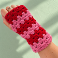 Pink and red handmade crochet wrist warmer being worn on a hand against a soft mint green background.
