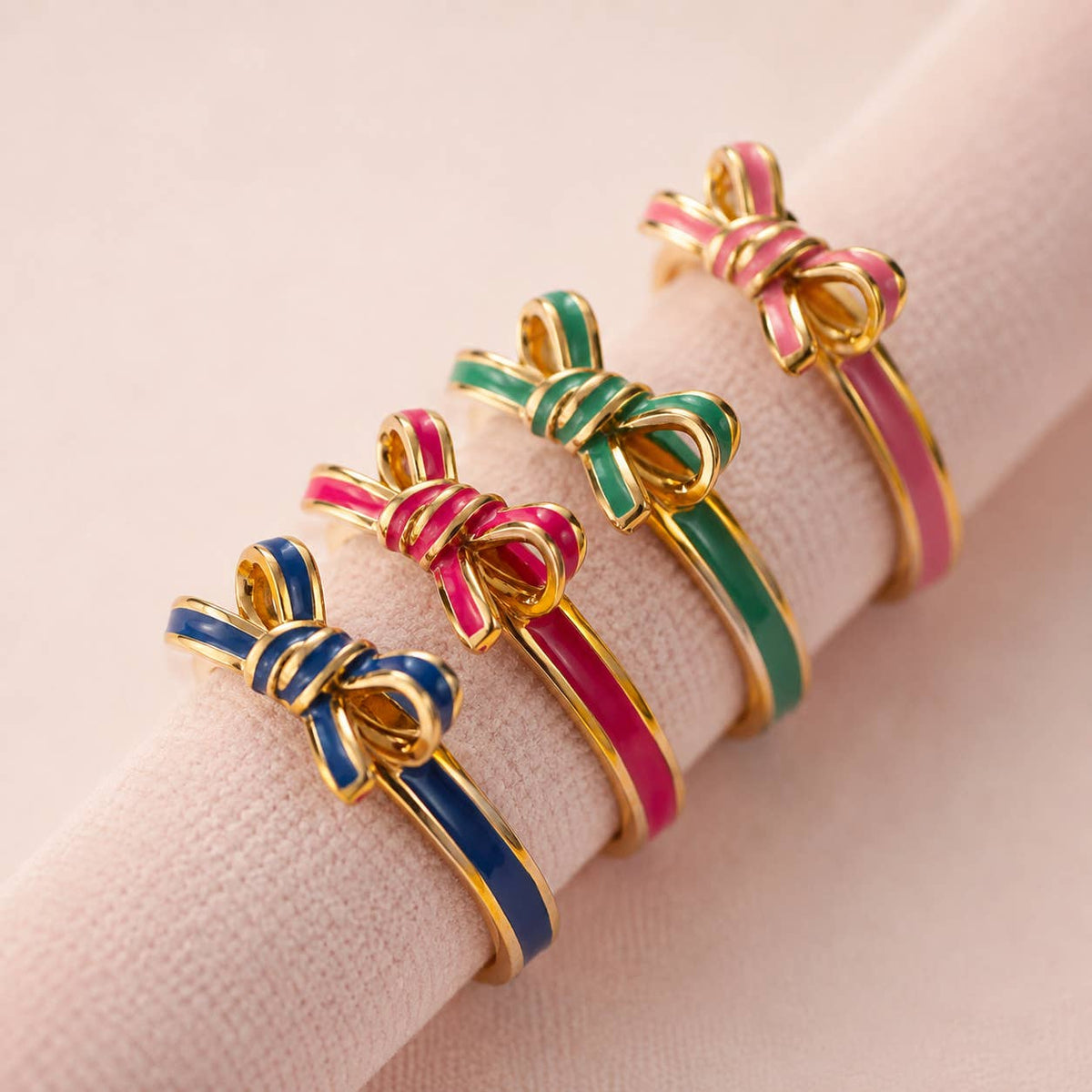 Blue, bright pink, green and pale pink enamel bow rings with glossy gold-tone bands displayed together.