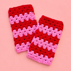 One of a kind pair of bright pink and red crochet wrist warmers laid on a soft pink background.
