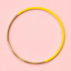 Yellow dip enamel stacking bangle with polished gold tone detailing on a pale pink background.