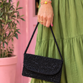 Woman in a green dress holding a small black beaded shoulder bag with a curved flap front.
