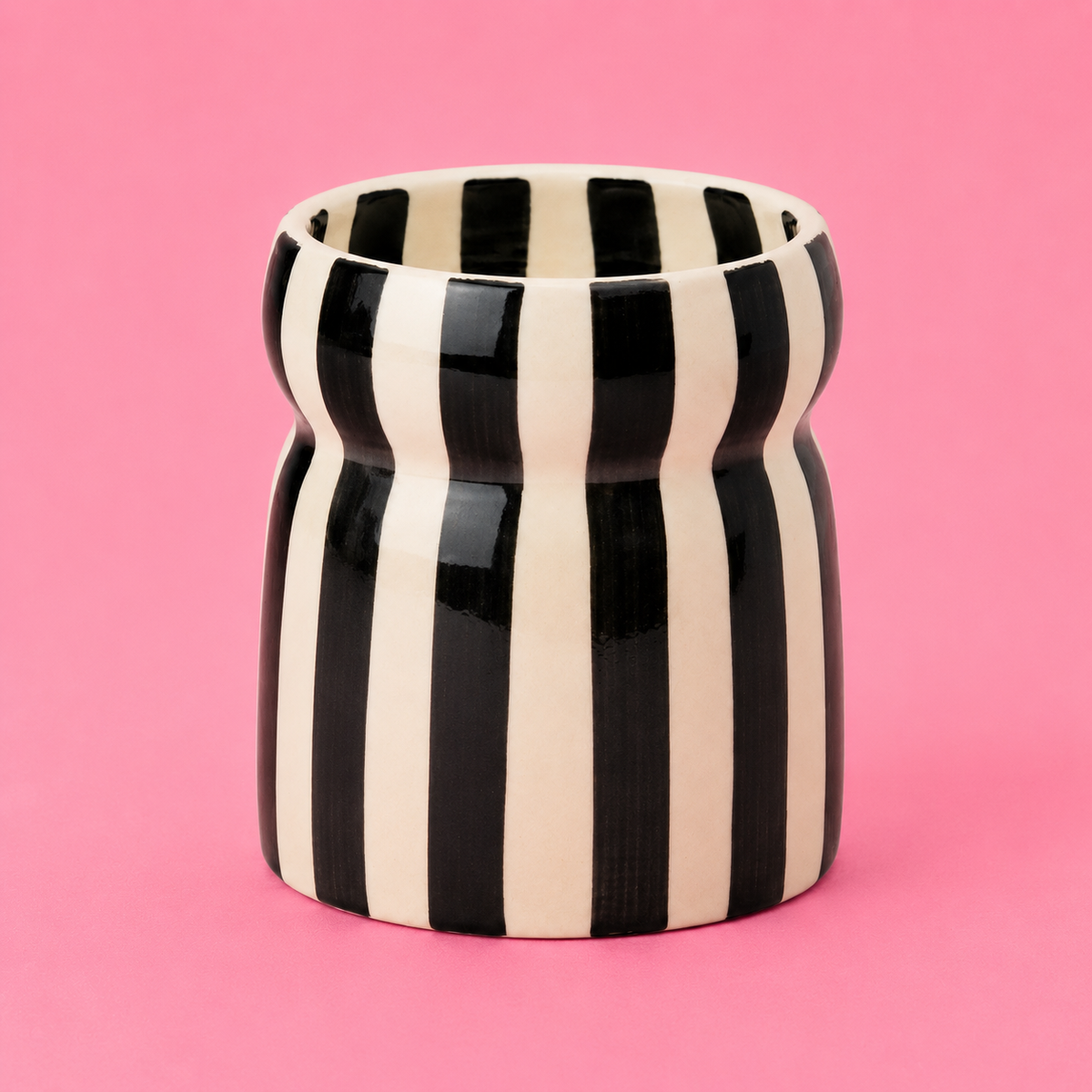 Close up of Cabana candle showing its striped ceramic vessel and pinched shape.