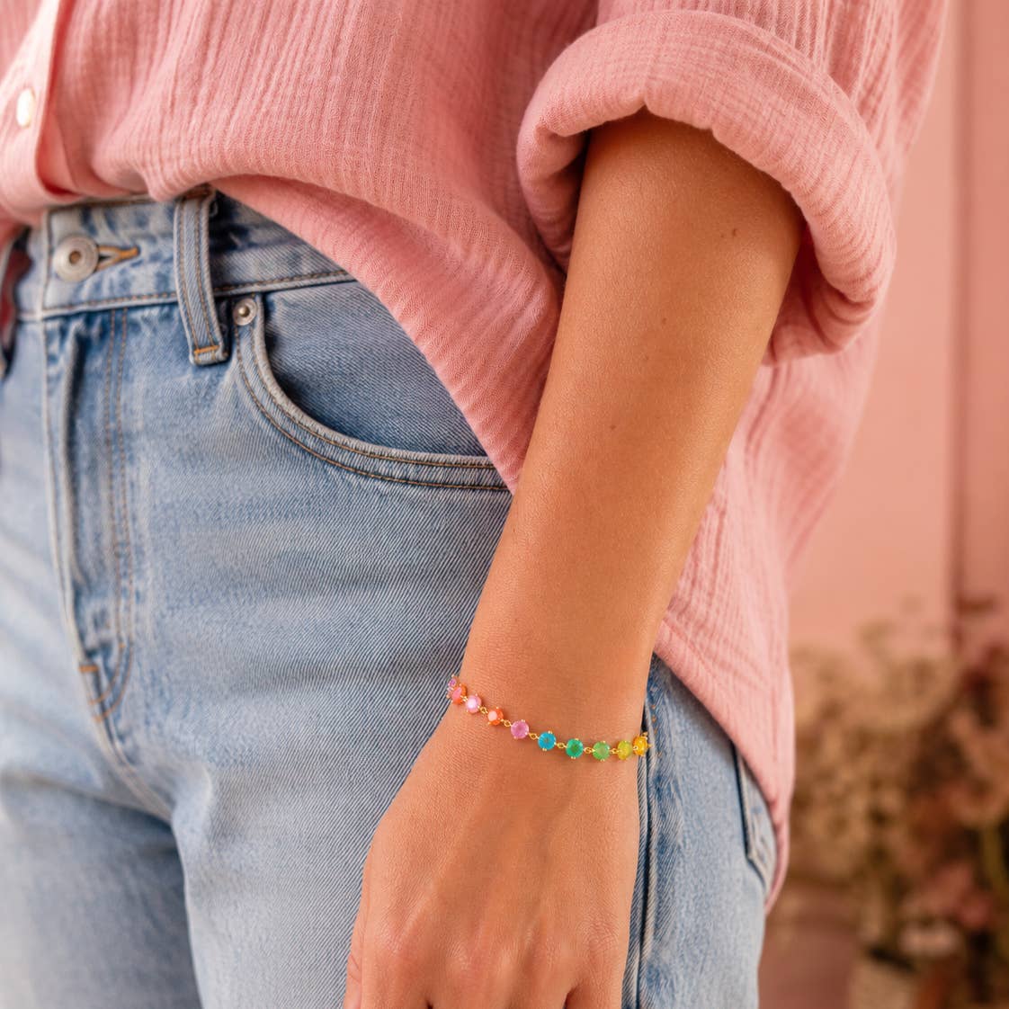 Rainbow frosted crystal gold chain bracelet worn on the wrist with a pink top and blue jeans.