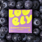 Blueberry Cheesecake Lip Balm in colourful purple packaging surrounded by fresh blueberries.